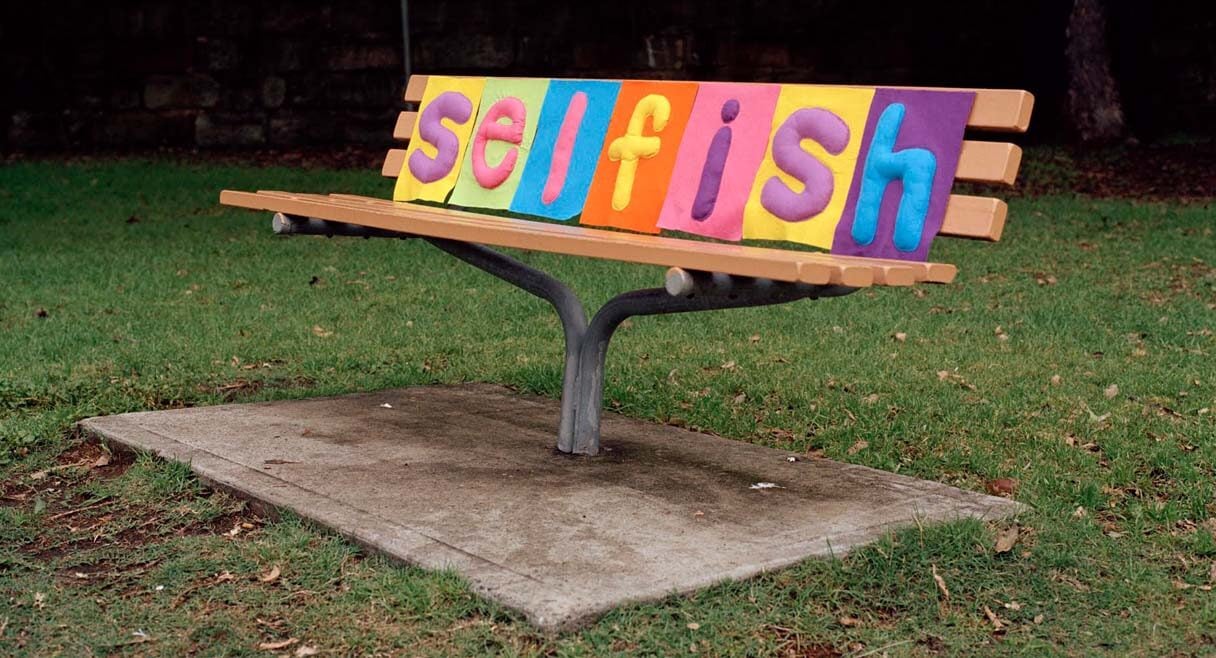 image of a park bench with the word selfish in coloured tiles sitting on it