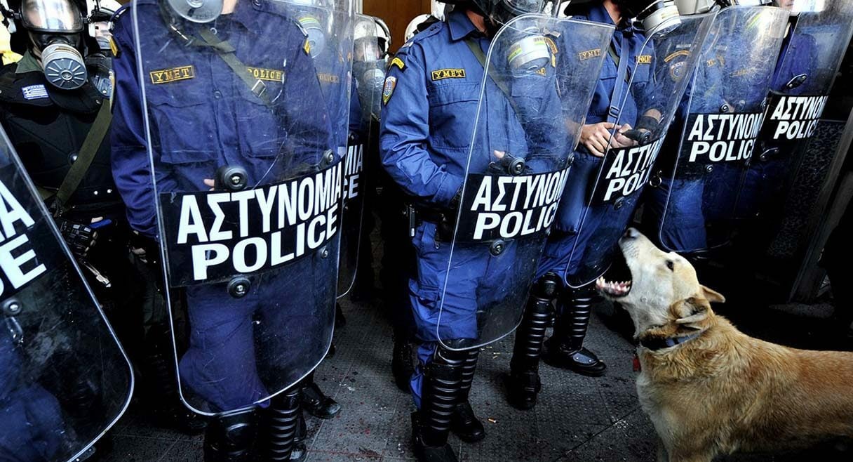 image of a dog sitting in front a row of riot police barking fiercely at them