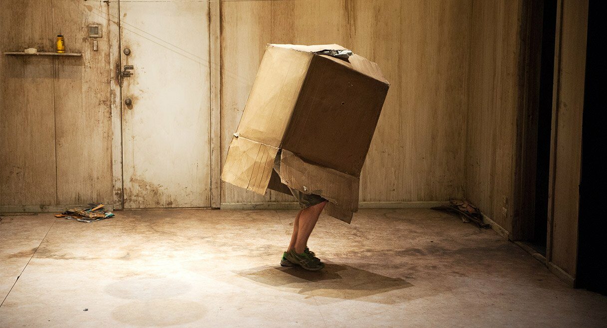 image of a box with a pair of a mans legs sticking out the bottom in a brown room