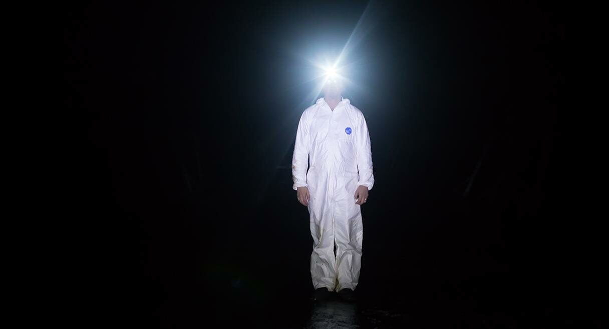 image of man in a white suit with a miners lamp on his head standing in a black space