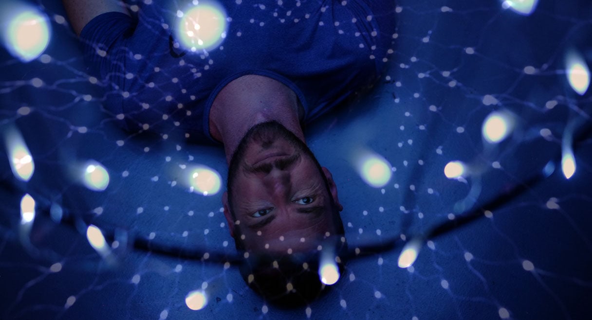 image of a man wearing a blue shirt lying in a light installation light reflects all over him