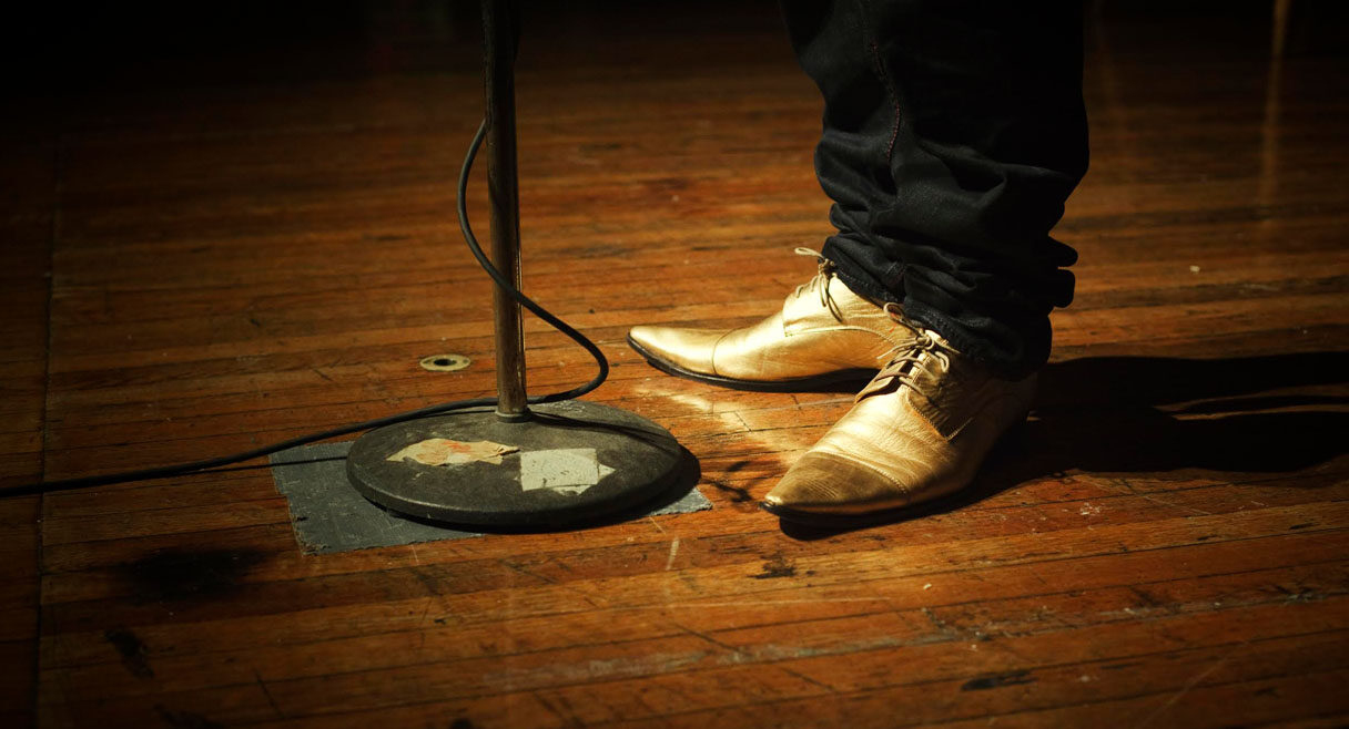 Image of a stage with a pair of gold shoes and a microphone stand