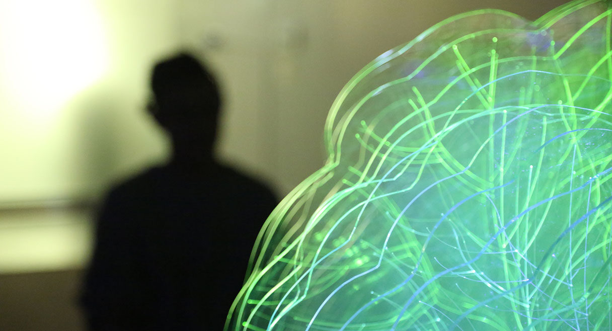 man in shadow with a green electrical bulb in the corner like a brain