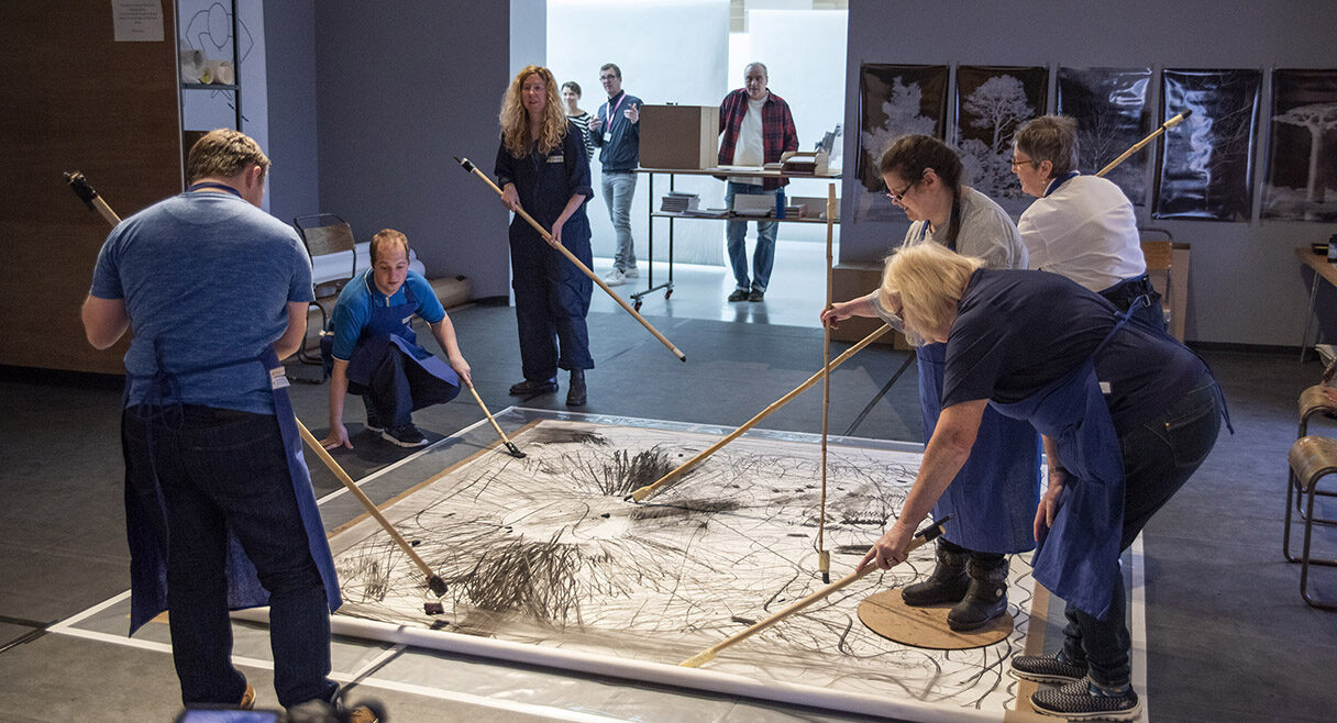 group of artists making art around a square mat in a gallery